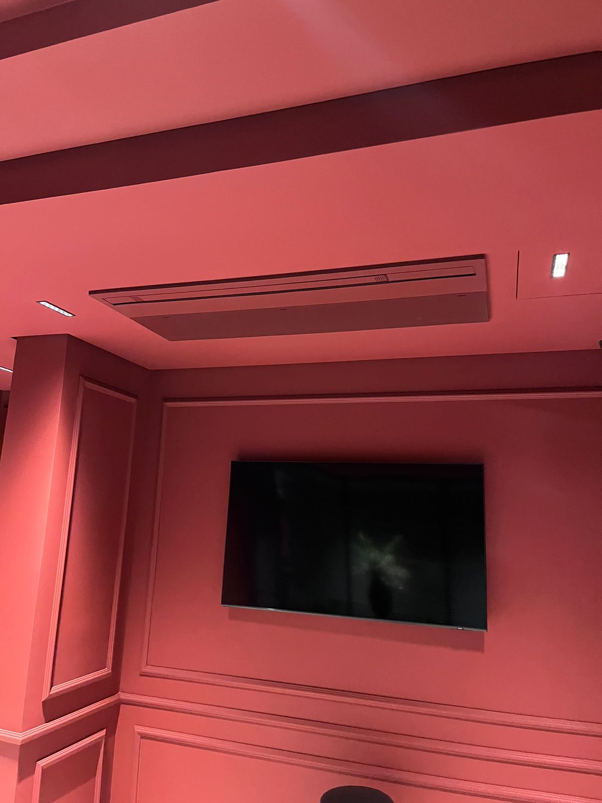 Cassete de teto pintado em tom rosé integrado ao teto e parede de uma sala de TV